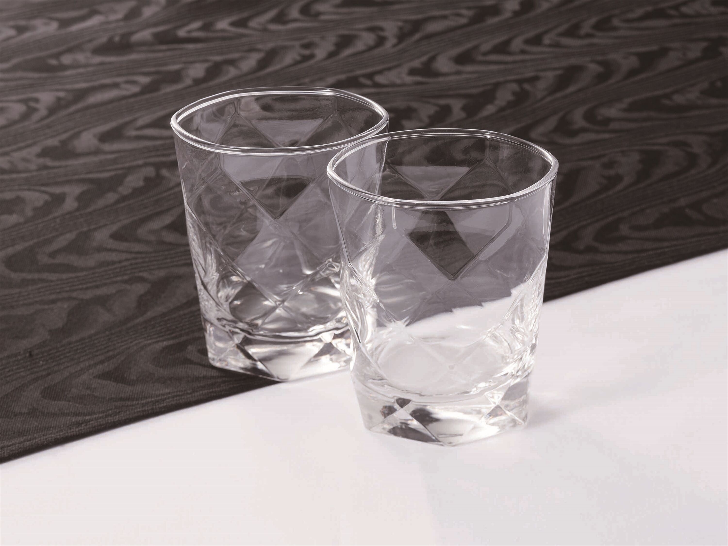Dos vasos de vidrio transparente sobre una superficie blanca con un fondo oscuro estampado.