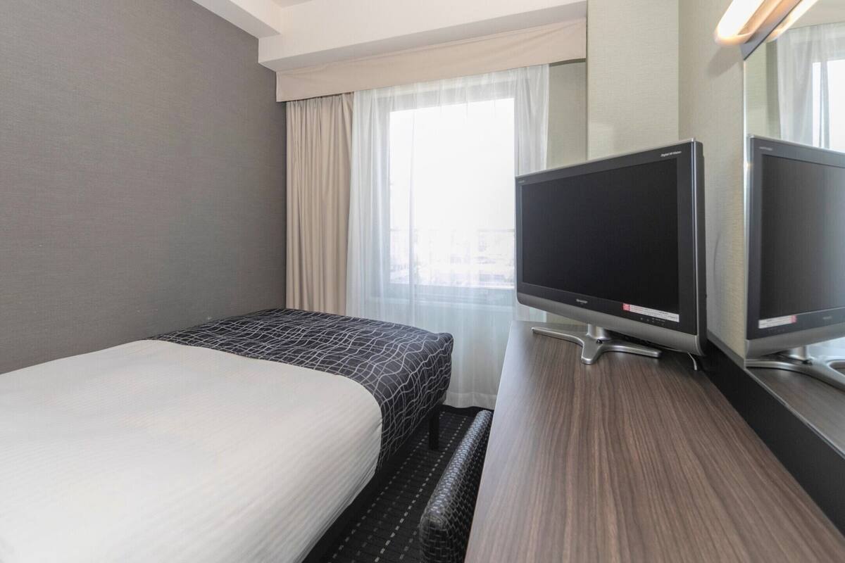 A hotel room with a bed, a TV, and a window with curtains.