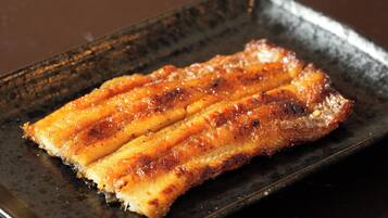 A rectangular plate with a grilled dish, possibly pork belly, on a dark, textured surface.