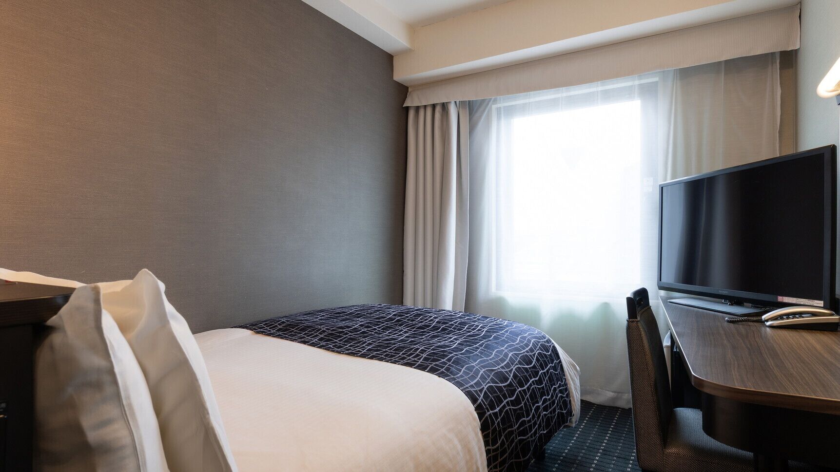 A hotel room with a bed, a desk, a television, and a window with curtains.