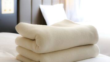 A neatly folded beige blanket on a bed with a white pillow and a headboard in the background.