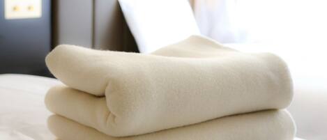 A neatly folded beige blanket on a bed with a white pillow and a headboard in the background.