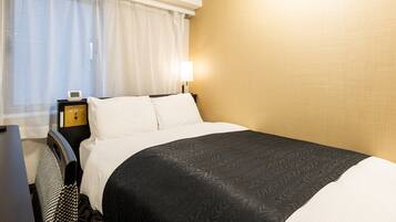 A hotel room with a bed, a bedside table, a lamp, and a window with curtains.
