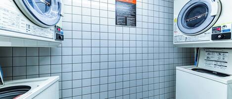 A laundry room with two washing machines, a dryer, and a tiled wall with a terms and conditions sign.