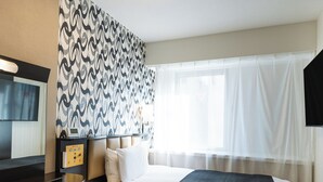 Ein Hotelzimmer mit einem großen Bett, einem Flachbildfernseher, einem Nachttisch mit Lampe und einer Wand mit Muster.