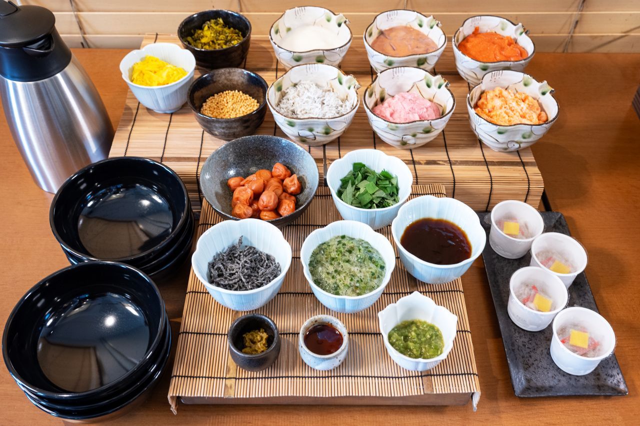 A variety of food items and condiments arranged on a table, including bowls of rice, vegetables, and sauces.