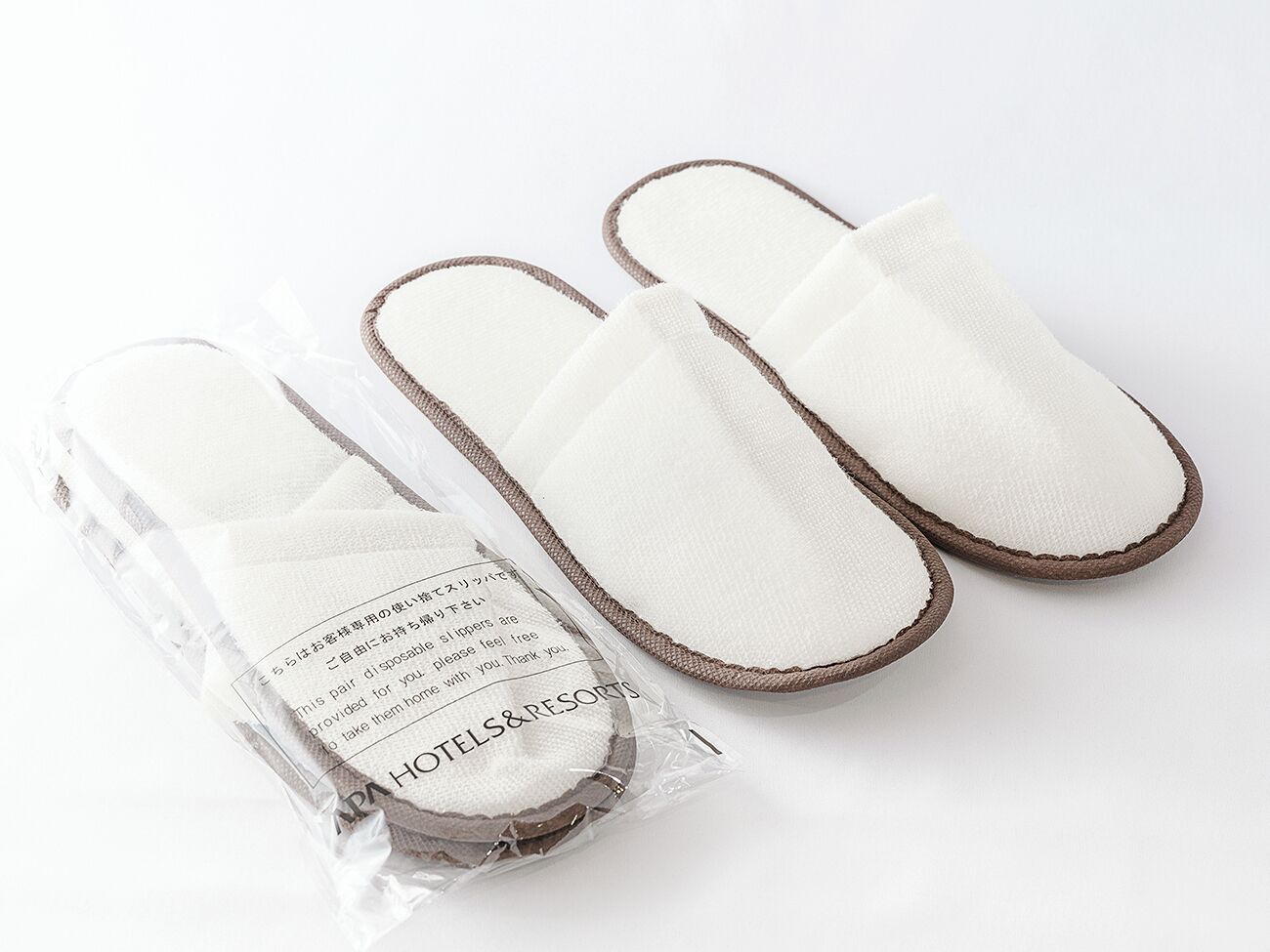 Um par de chinelos brancos com detalhes marrons, embalados em um saco plástico transparente com etiqueta.