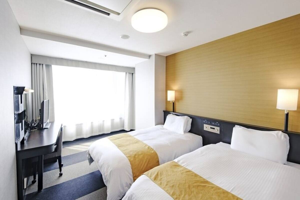 Une chambre d’hôtel avec deux lits, un bureau, une chaise, une télévision et une fenêtre avec des rideaux.