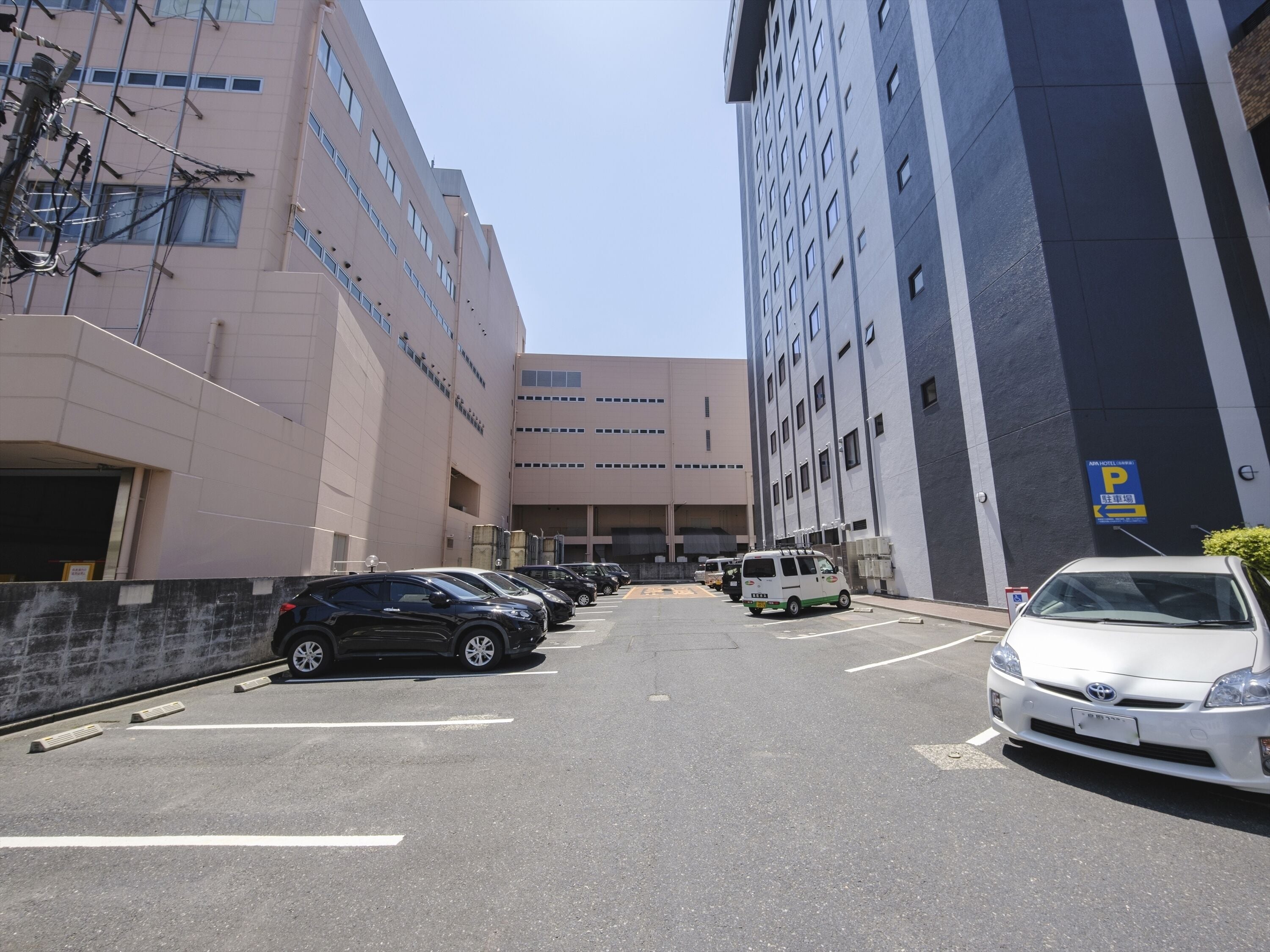 Un estacionamiento con varios coches y una furgoneta, junto a un edificio con un letrero que indica un hotel.