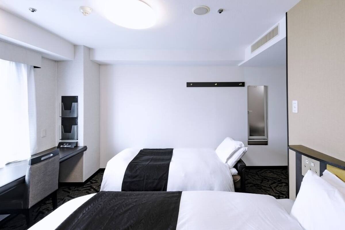Une chambre d’hôtel avec deux lits, un bureau, un réfrigérateur, un miroir et une fenêtre.
