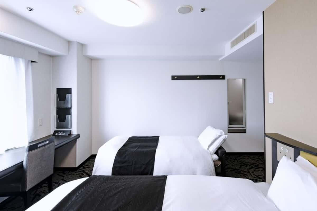 Une chambre d’hôtel avec deux lits, un bureau, un réfrigérateur, un miroir et une fenêtre.