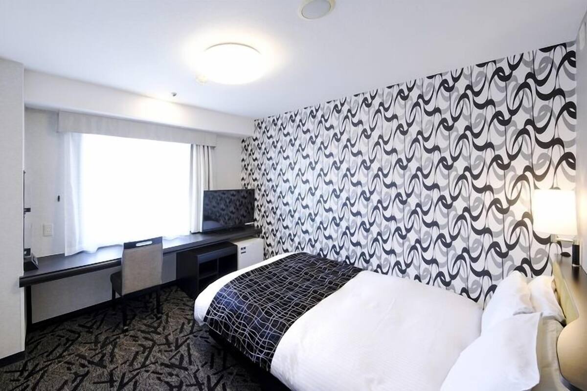 Une chambre d’hôtel avec un lit, un bureau, une chaise, une télévision et un mur décoré d’un motif.