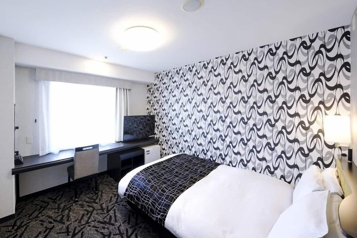 Une chambre d’hôtel avec un lit, un bureau, une chaise, une télévision et un mur décoré d’un motif.