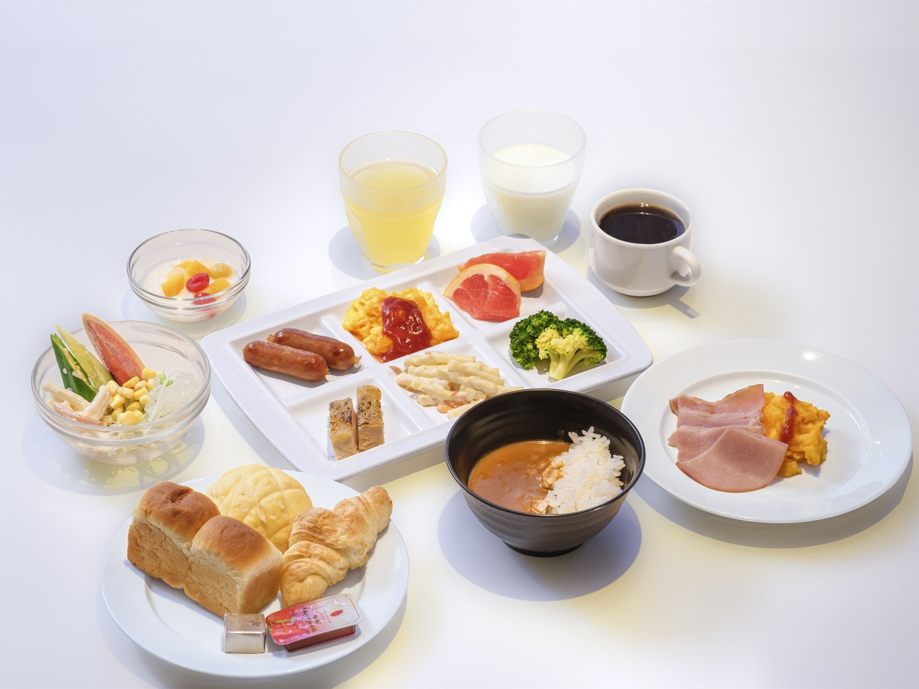 A breakfast spread with various dishes including sausages, scrambled eggs, toast, and a bowl of rice.