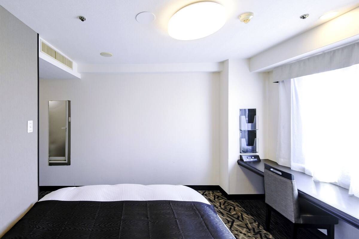 Une chambre d’hôtel avec un lit, un bureau, une chaise, une fenêtre et un miroir.