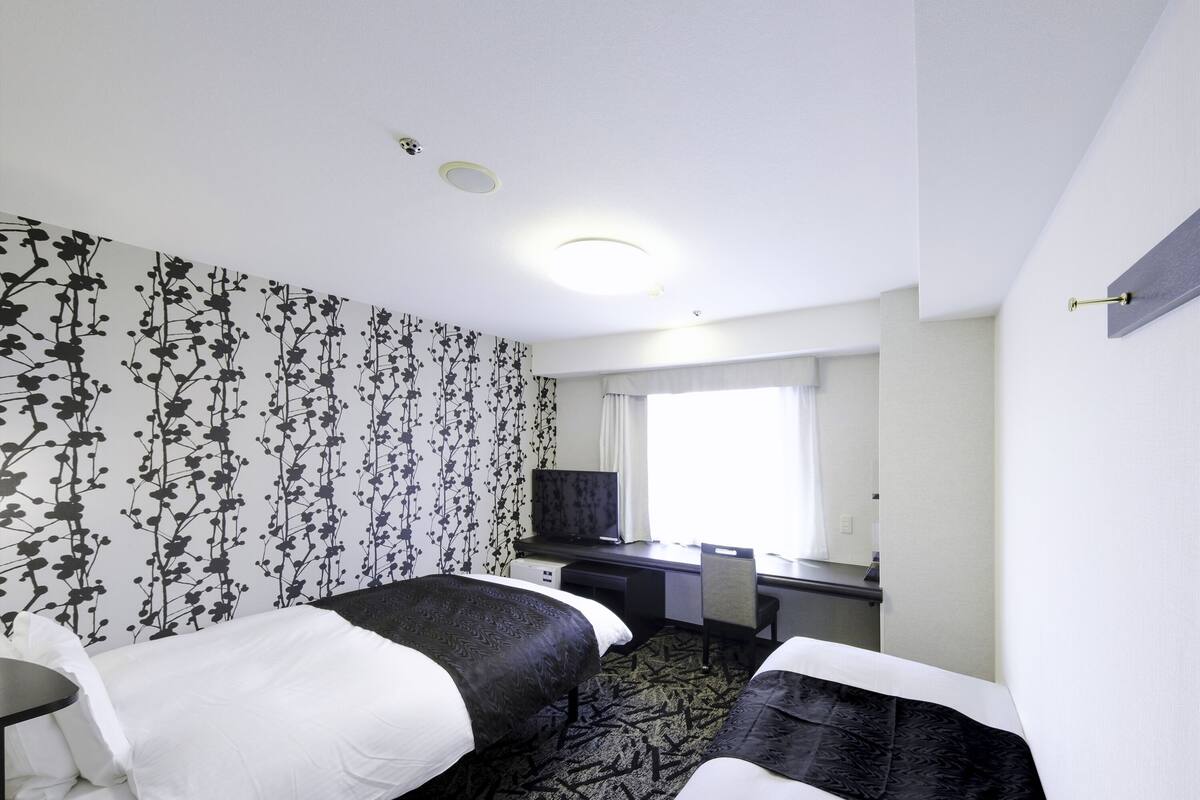 Une chambre d’hôtel avec deux lits, un bureau, une télévision et une fenêtre avec des rideaux.