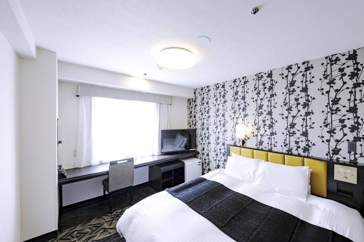 Une chambre d’hôtel équipée d’un lit, d’un bureau, d’une chaise, d’une télévision et d’une fenêtre avec des rideaux.
