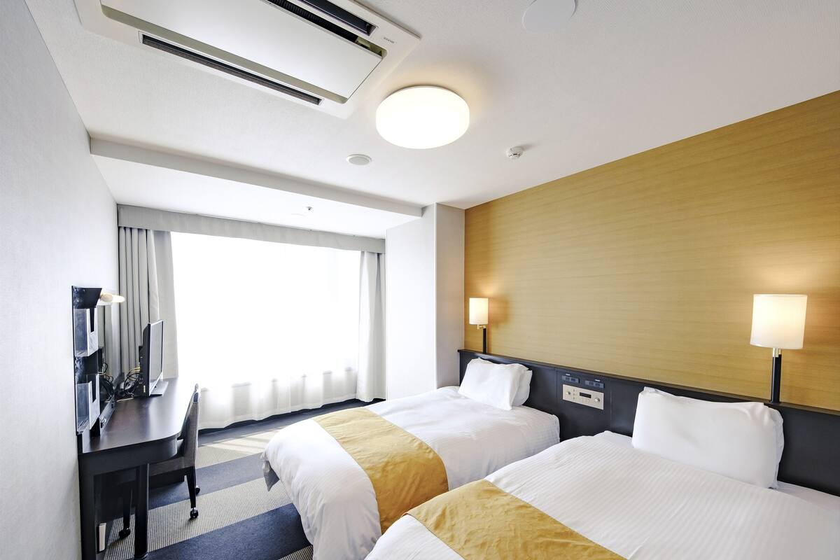 Une chambre d’hôtel avec deux lits, un bureau, une chaise, une télévision et une fenêtre avec des rideaux.