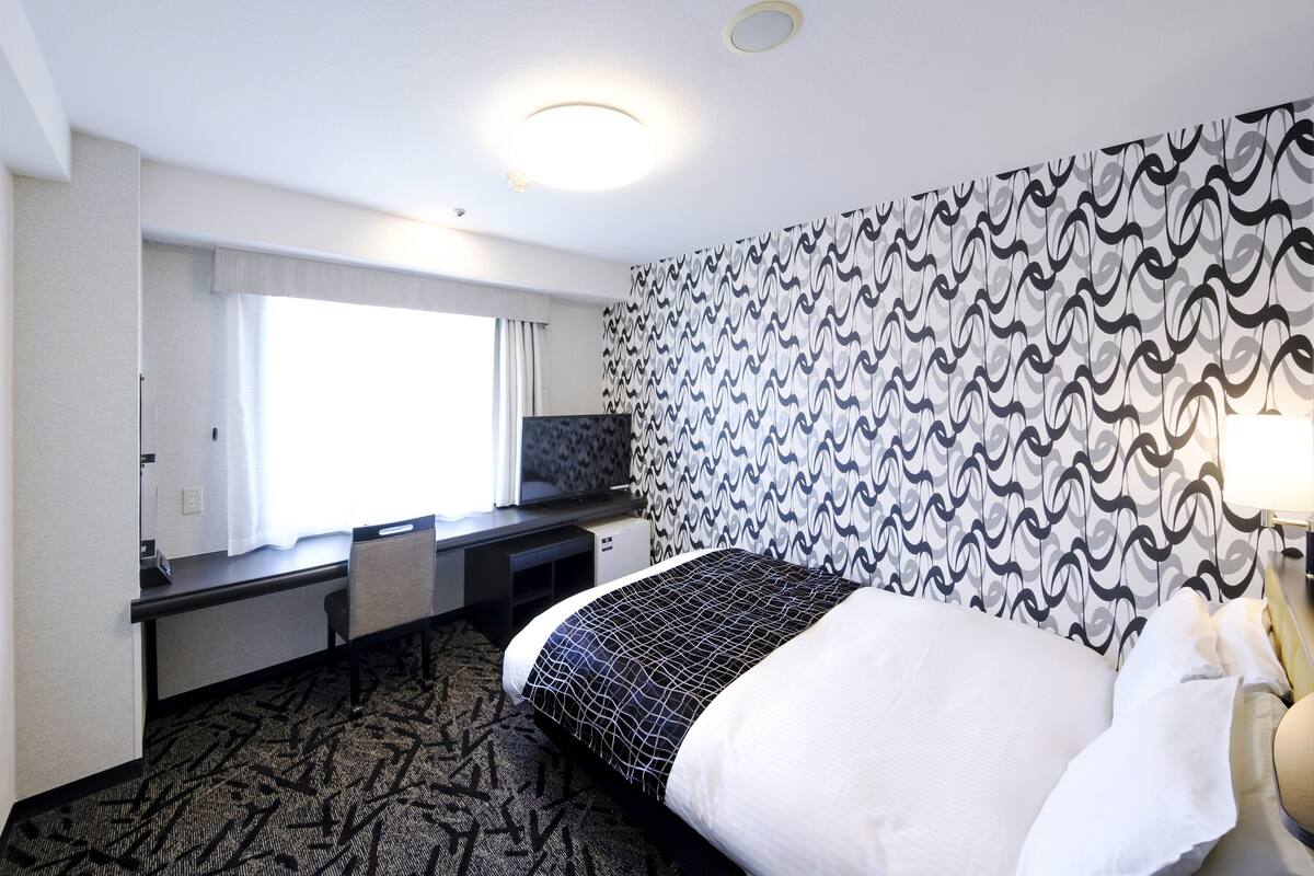 Une chambre d’hôtel avec un lit, un bureau, une chaise et un mur décoré de motifs.