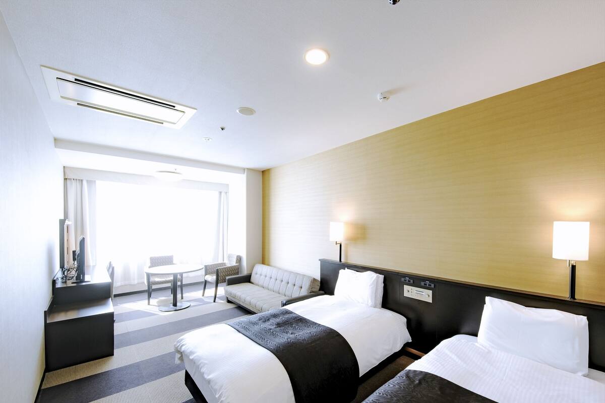 Une chambre d’hôtel avec deux lits, un bureau, une chaise et une grande fenêtre.