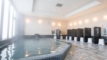 Una amplia piscina cubierta con paredes y suelo de baldosas, rodeada de varios cubículos de ducha.