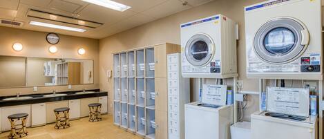 A public laundry facility with multiple washing machines, a mirror, and a clock on the wall.