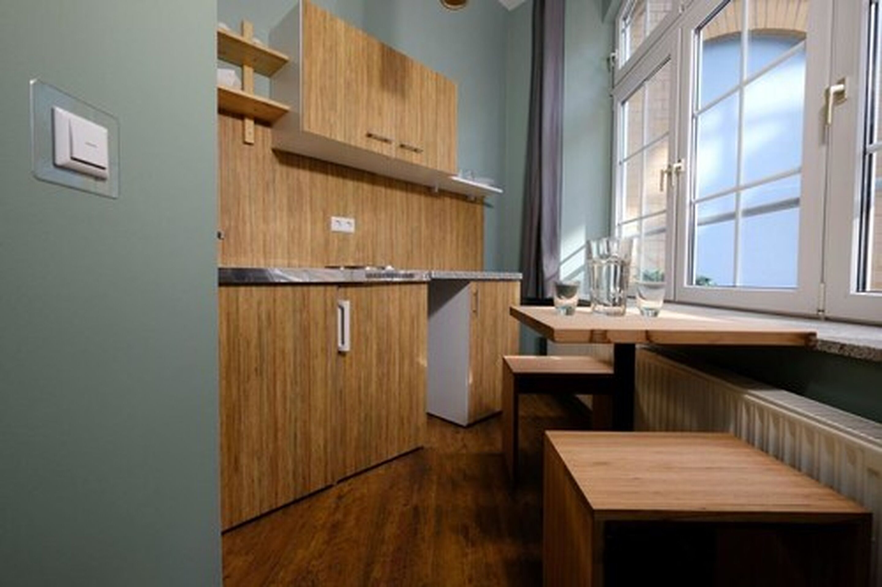 Eine kleine Küche mit Holzschränken, einem kleinen Kühlschrank und einem Fenster mit Vorhängen.