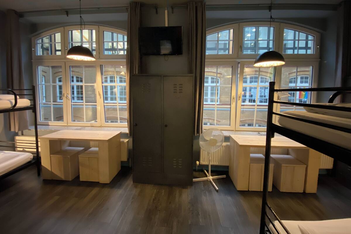 A dormitory room with bunk beds, a desk, and a radiator.