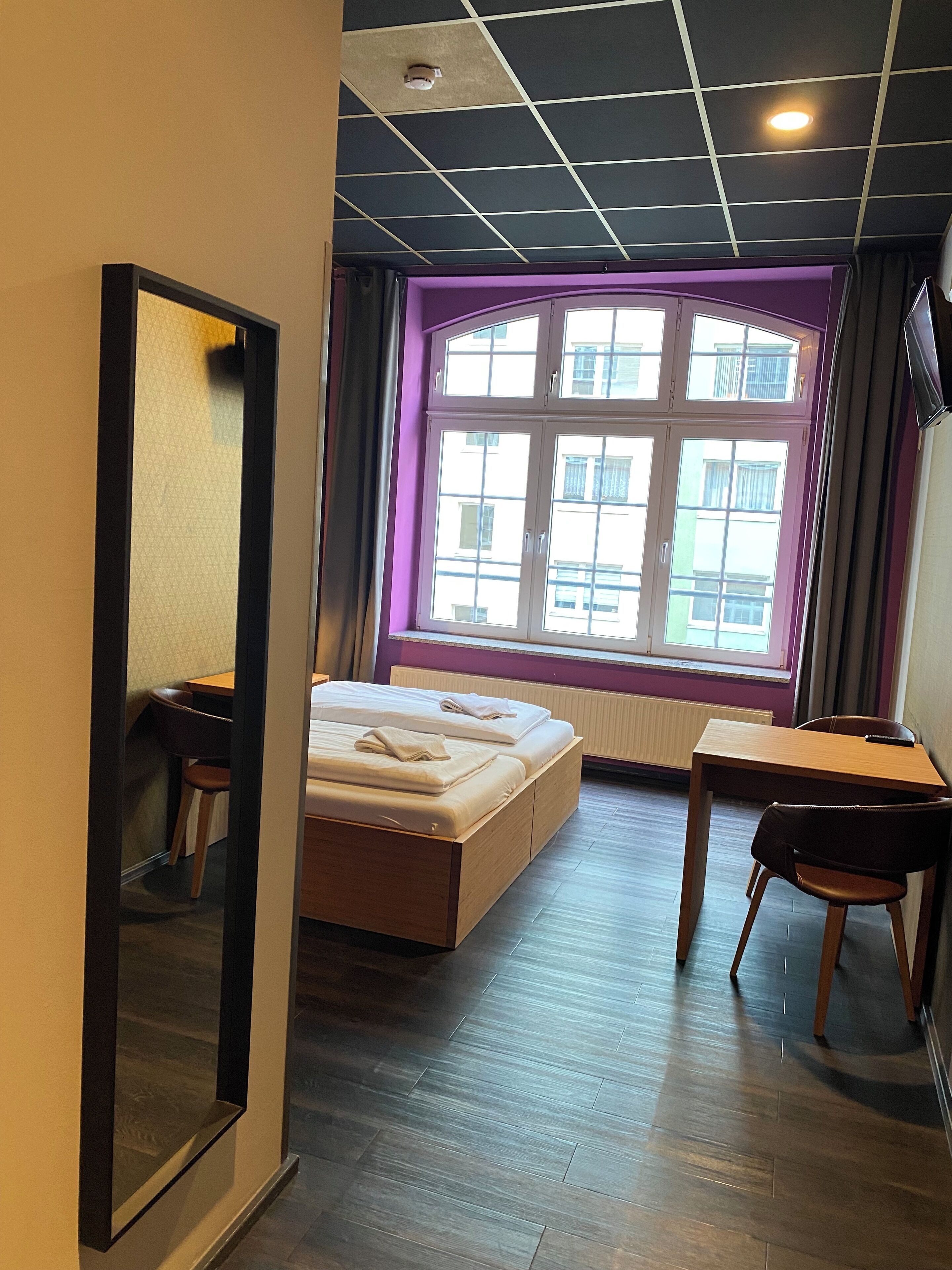 Ein Hotelzimmer mit Bett, Schreibtisch und einem Fenster mit Blick auf Gebäude.