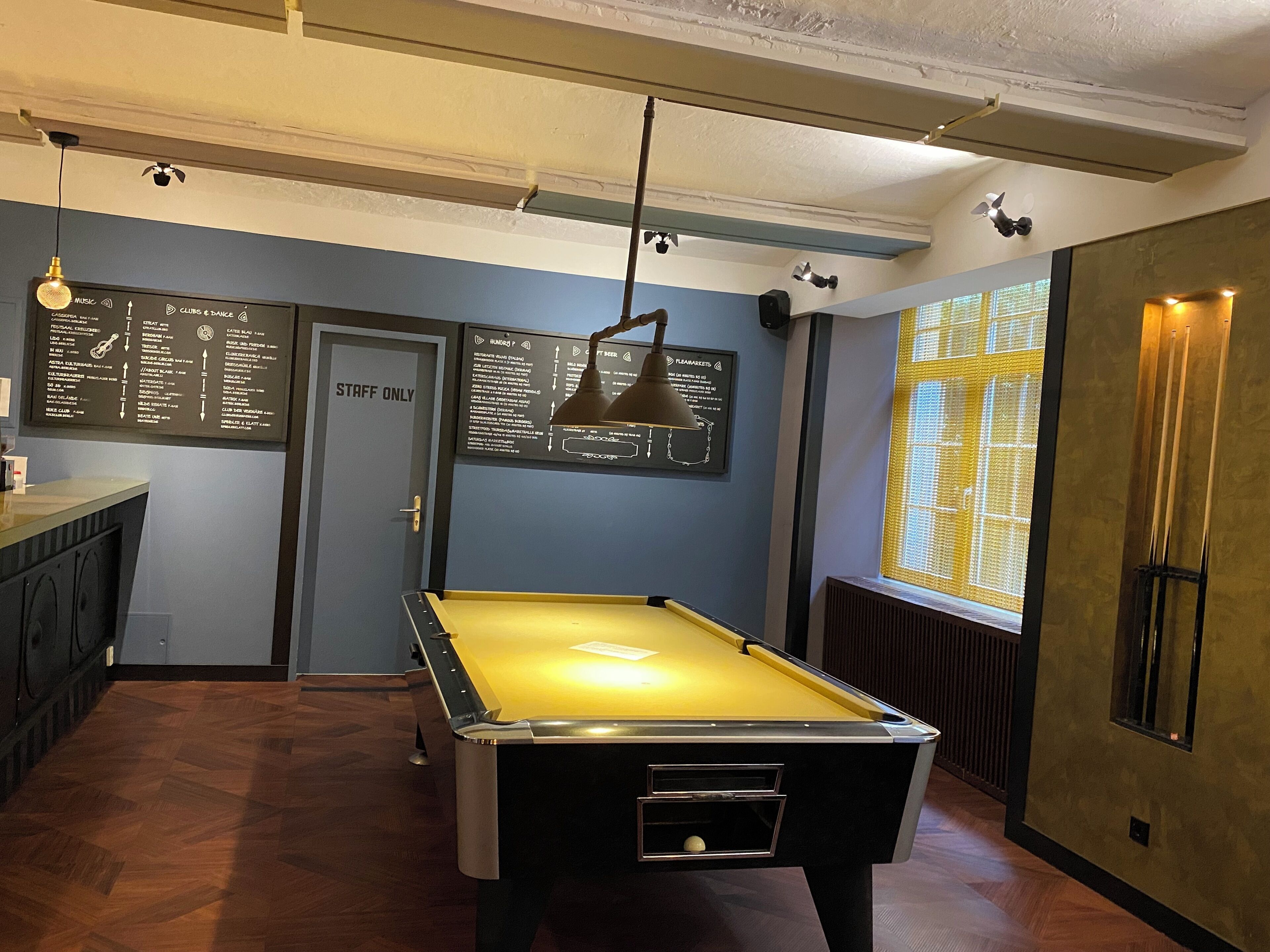 A pool table in a room with a 'STAFF ONLY' door, a menu board, and a window with blinds.