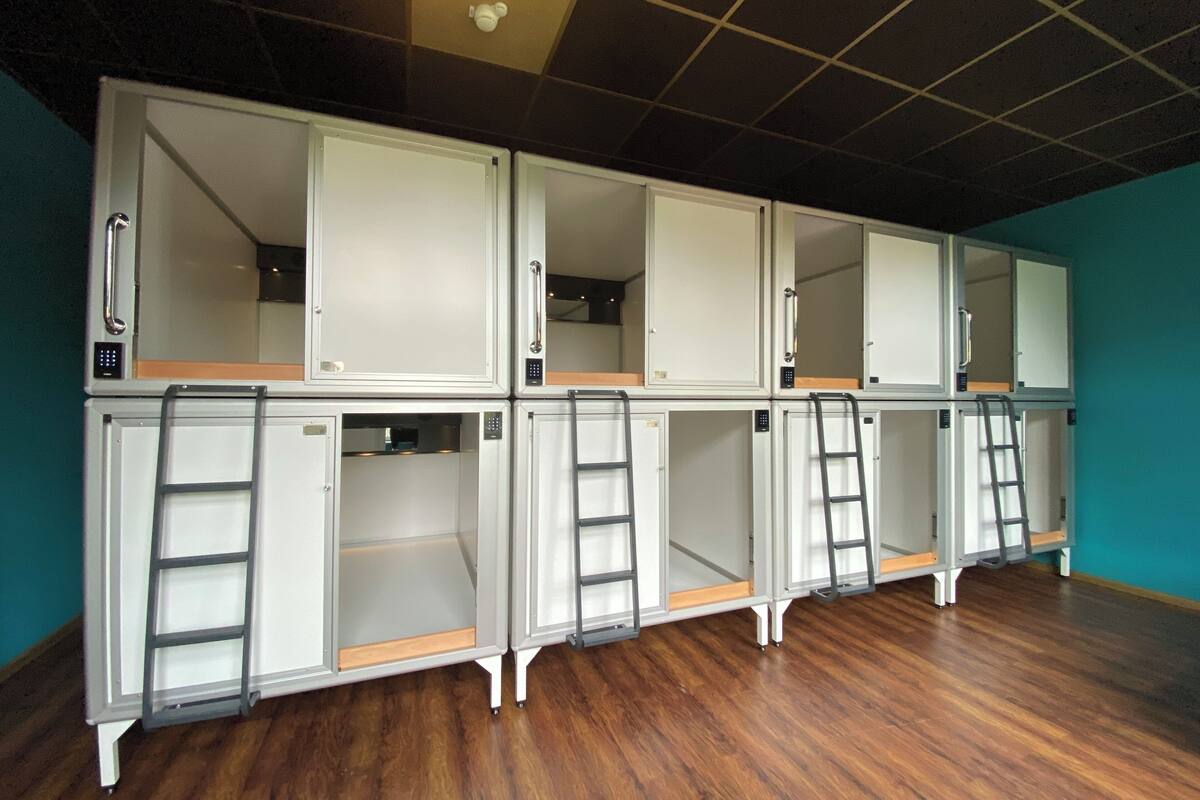 A row of bunk beds with individual lockers and ladders, in a room with wooden flooring and teal walls.