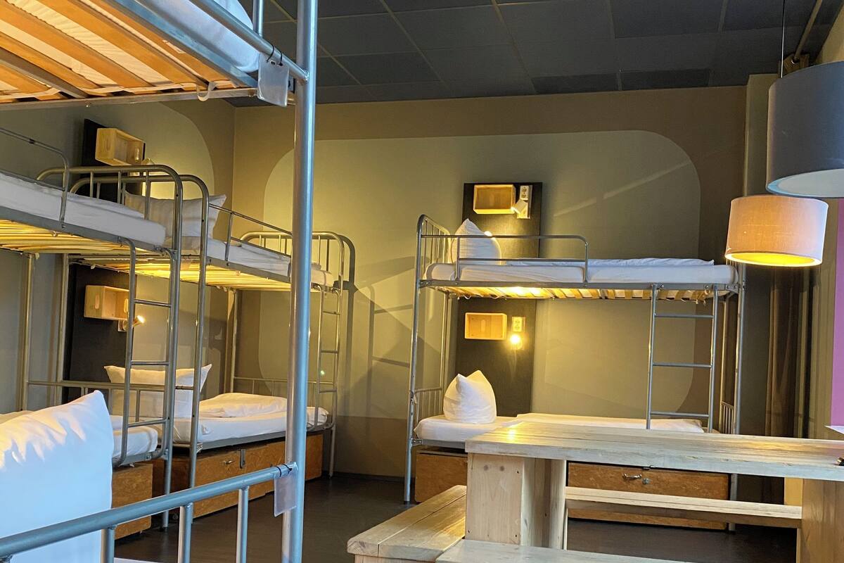 A dormitory room with bunk beds, a wooden desk, and a lamp.