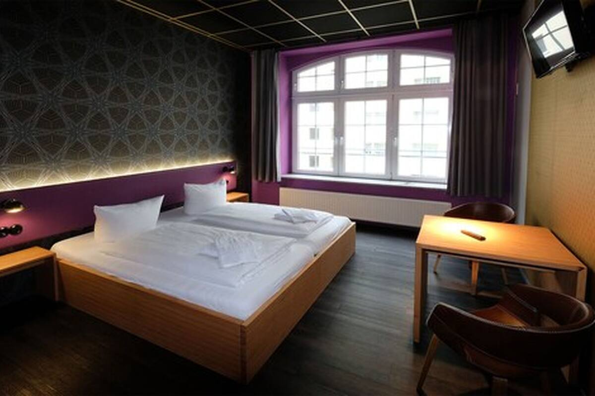 A hotel room with a large bed, a desk, and a chair.