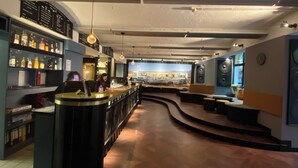 A bar area with a counter, shelves with bottles, and a seating area with a mural in the background. - Singer109 Hostel (Berlin)