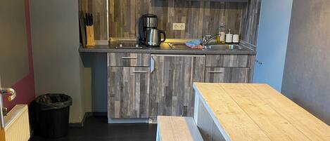 A compact kitchen with wooden cabinets, a coffee maker, and a bench.
