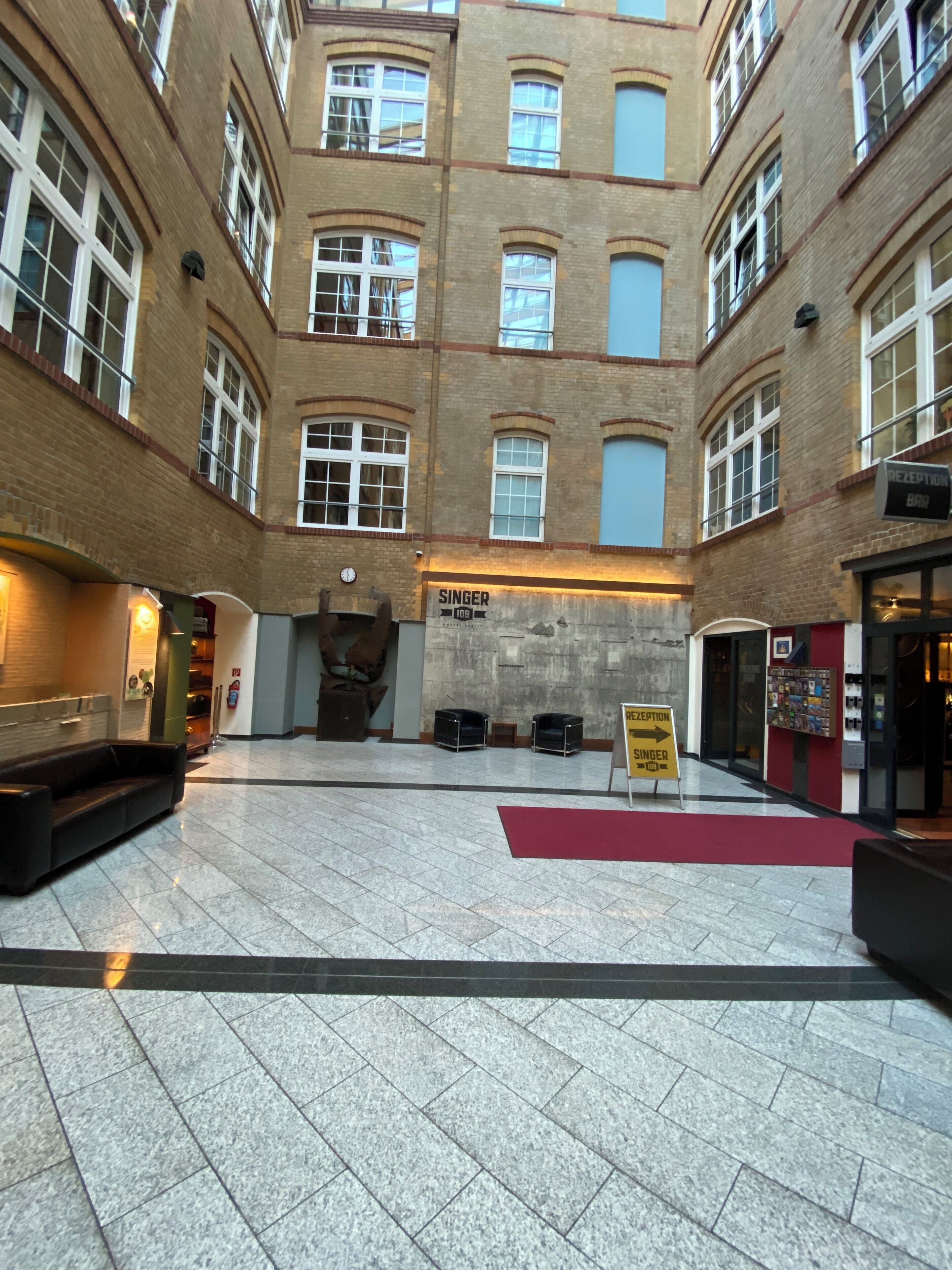 Ein geräumiges Atrium mit Empfangsbereich, einer Bar und einem Schild mit der Aufschrift 'SINGER 109'.