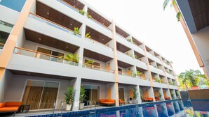 Un hotel de varios pisos con piscina, balcones con plantas y zonas de estar anaranjadas.