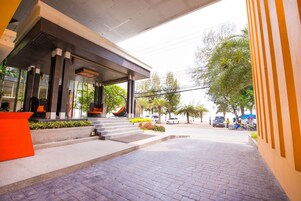 Un edificio moderno con un vestíbulo cubierto, escalones de acceso y una zona pavimentada en la parte frontal.