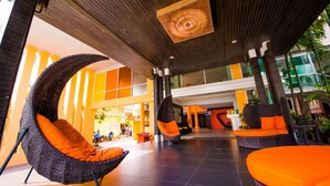 Un vestíbulo amplio con modernas sillas de mimbre y cojines naranja, un gran ventilador de techo y vistas al área exterior.