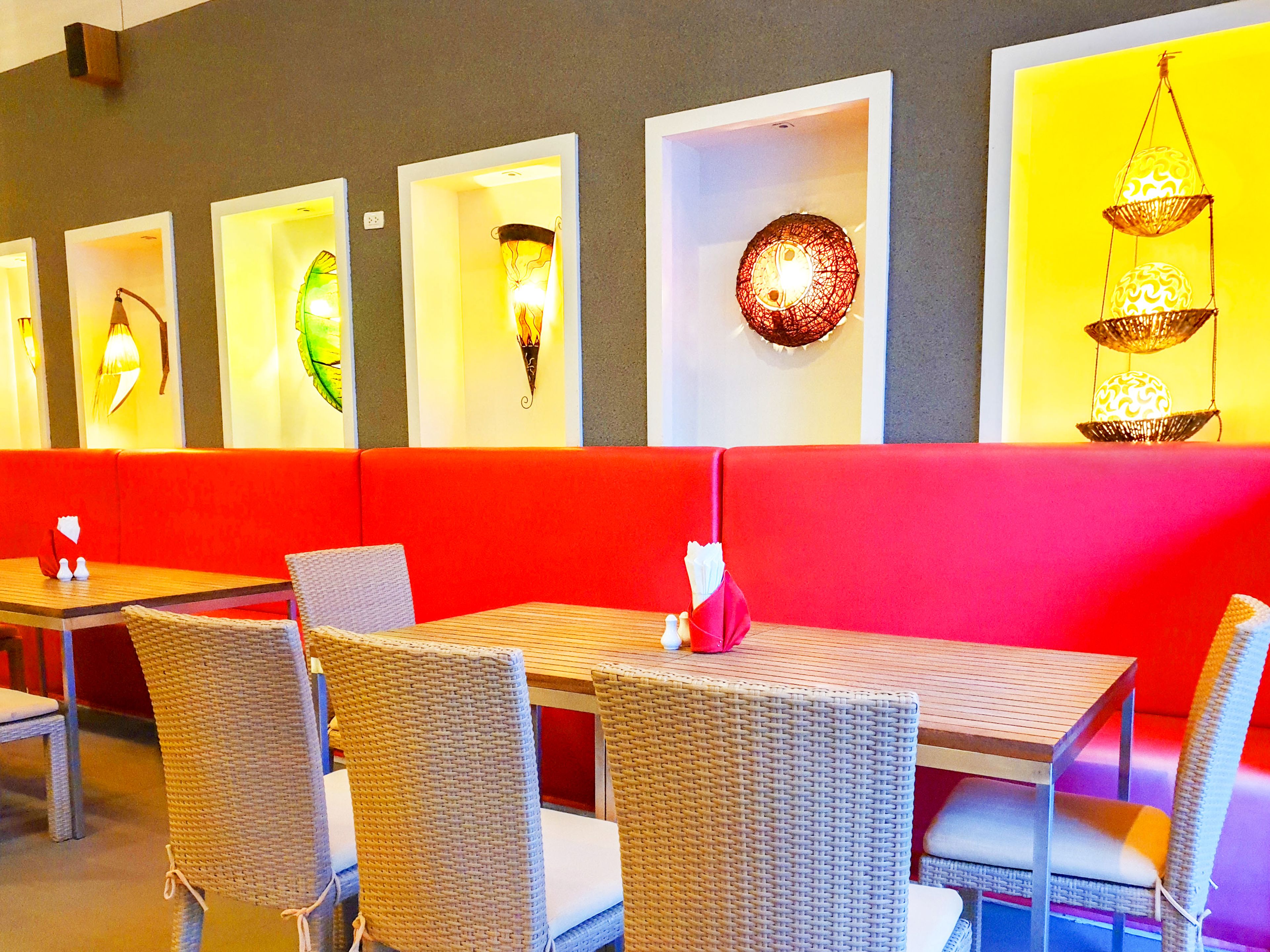 Un restaurant avec des banquettes rouges, des chaises en osier et des tables.