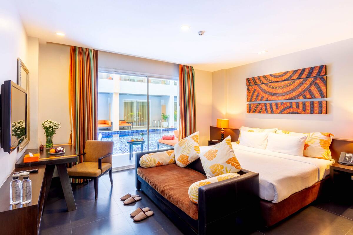 Habitación de hotel con cama, escritorio, silla, televisión y vista a la piscina.