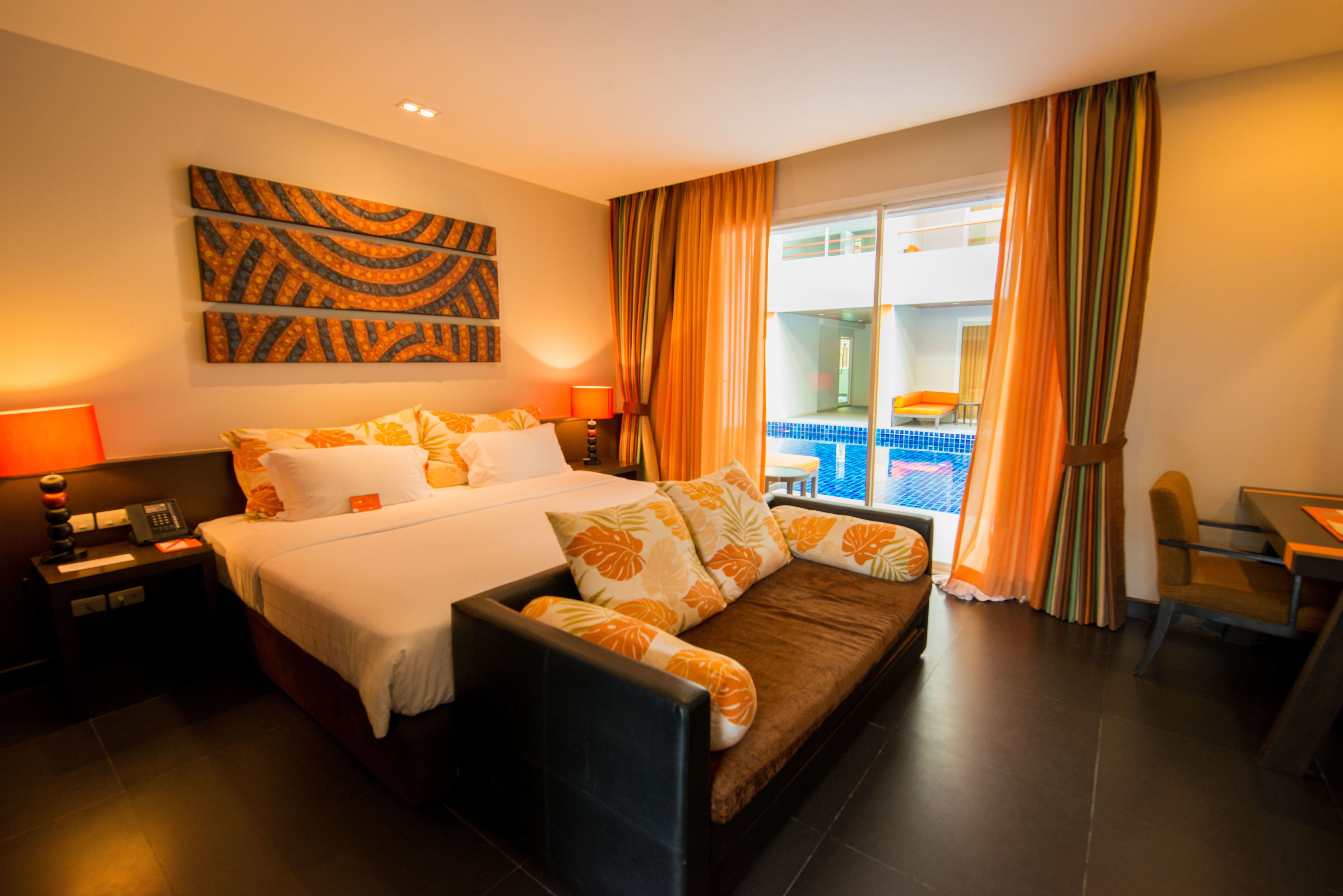 A hotel room with a bed, a sofa, a desk, and a view of a pool.