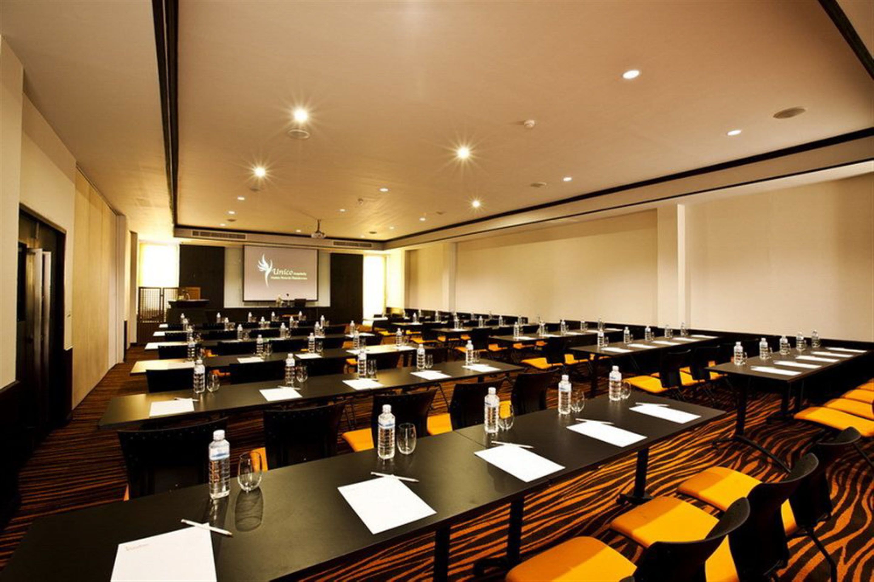 Une salle de conférence équipée de plusieurs tables, de chaises et d’un écran de projection.