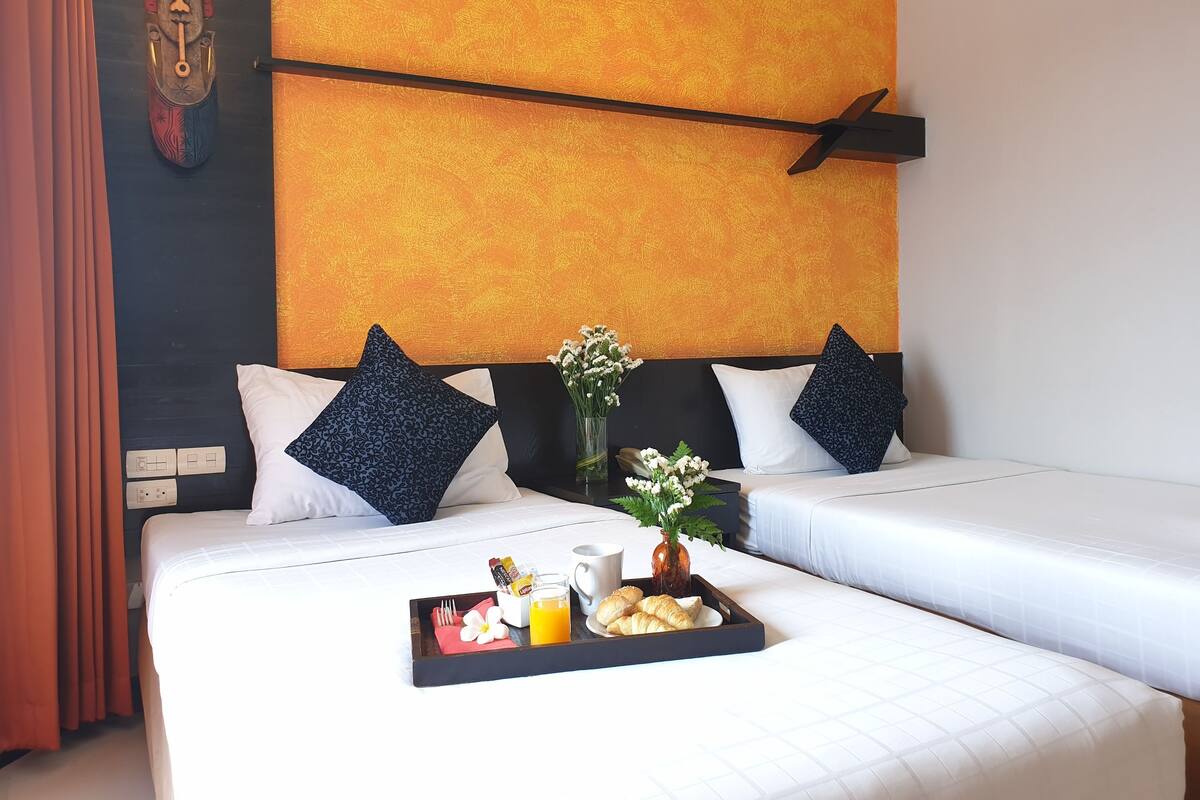 Una habitación de hotel con dos camas, una bandeja con alimentos para el desayuno y una máscara decorativa en la pared.