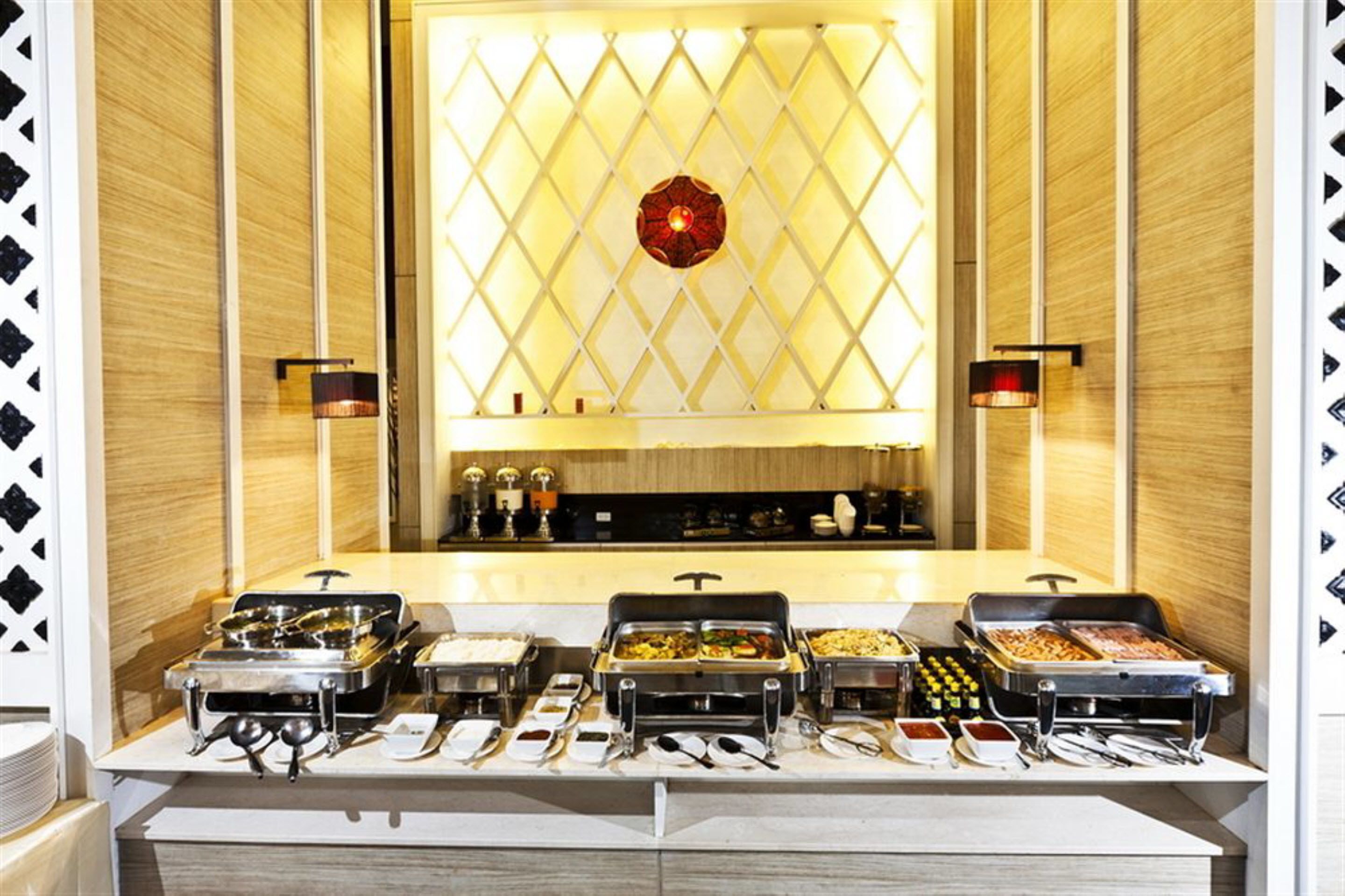 A buffet setup with various food stations, a central decorative light, and wall-mounted sconces.