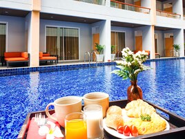 Una bandeja de desayuno junto a la piscina con croissants, tomates, jugo y leche, además de un florero con flores.