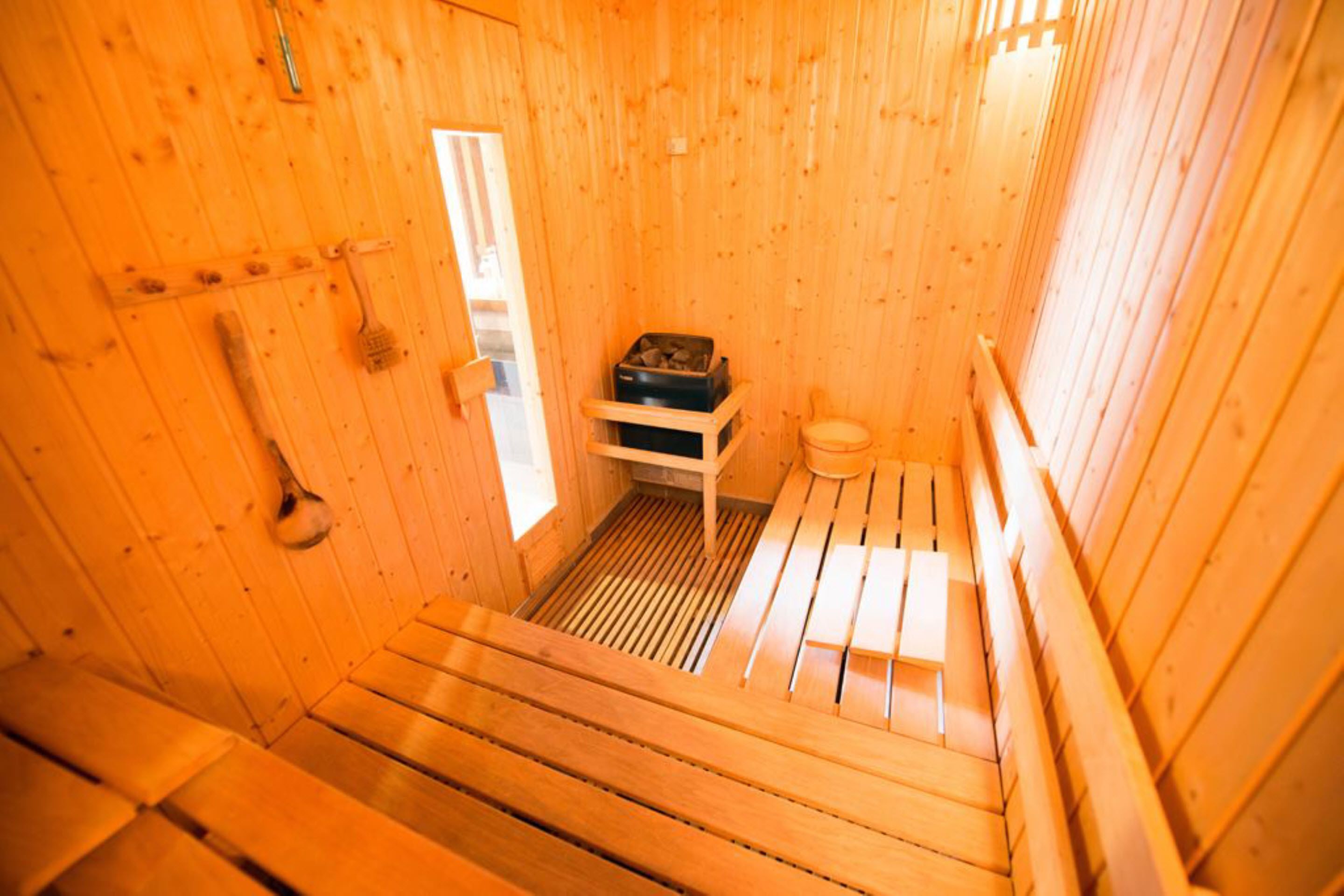 A sauna with wooden benches and a bench seat, a small shelf with a heater, and a toilet.