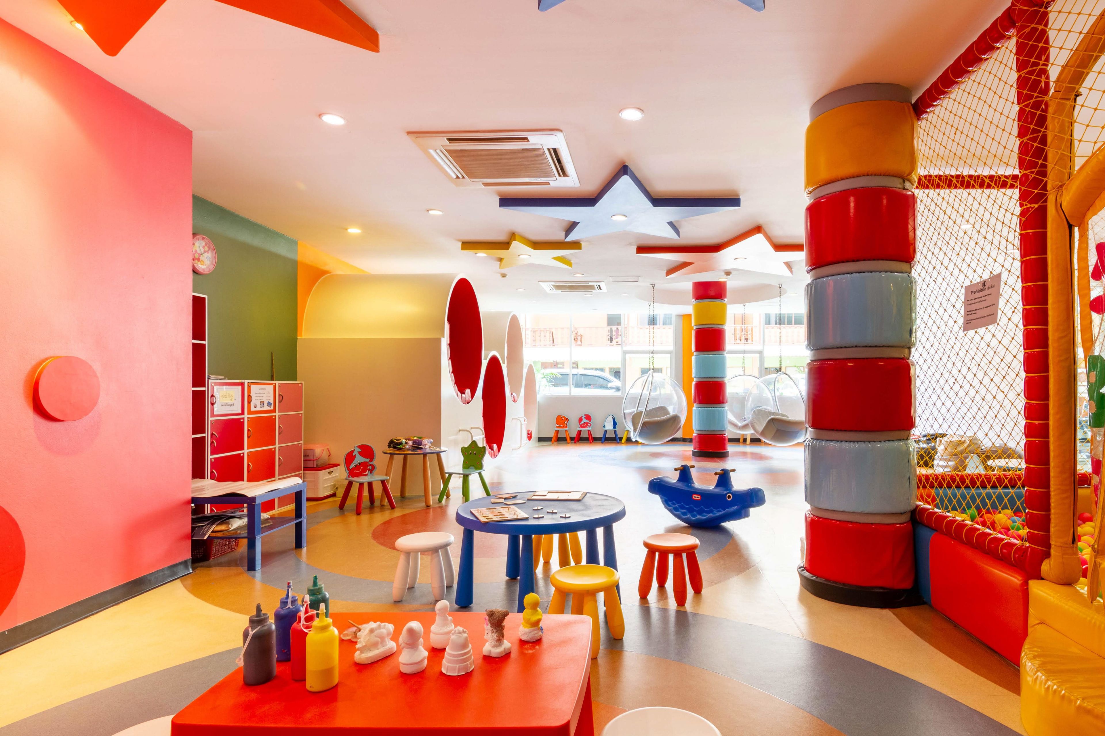 Un espace de jeux coloré pour enfants, équipé de tables, de chaises et d’une piscine à balles.