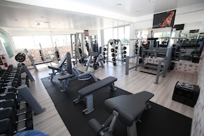 Academia com diversos equipamentos de exercícios, incluindo halteres, máquinas de musculação e bancos.