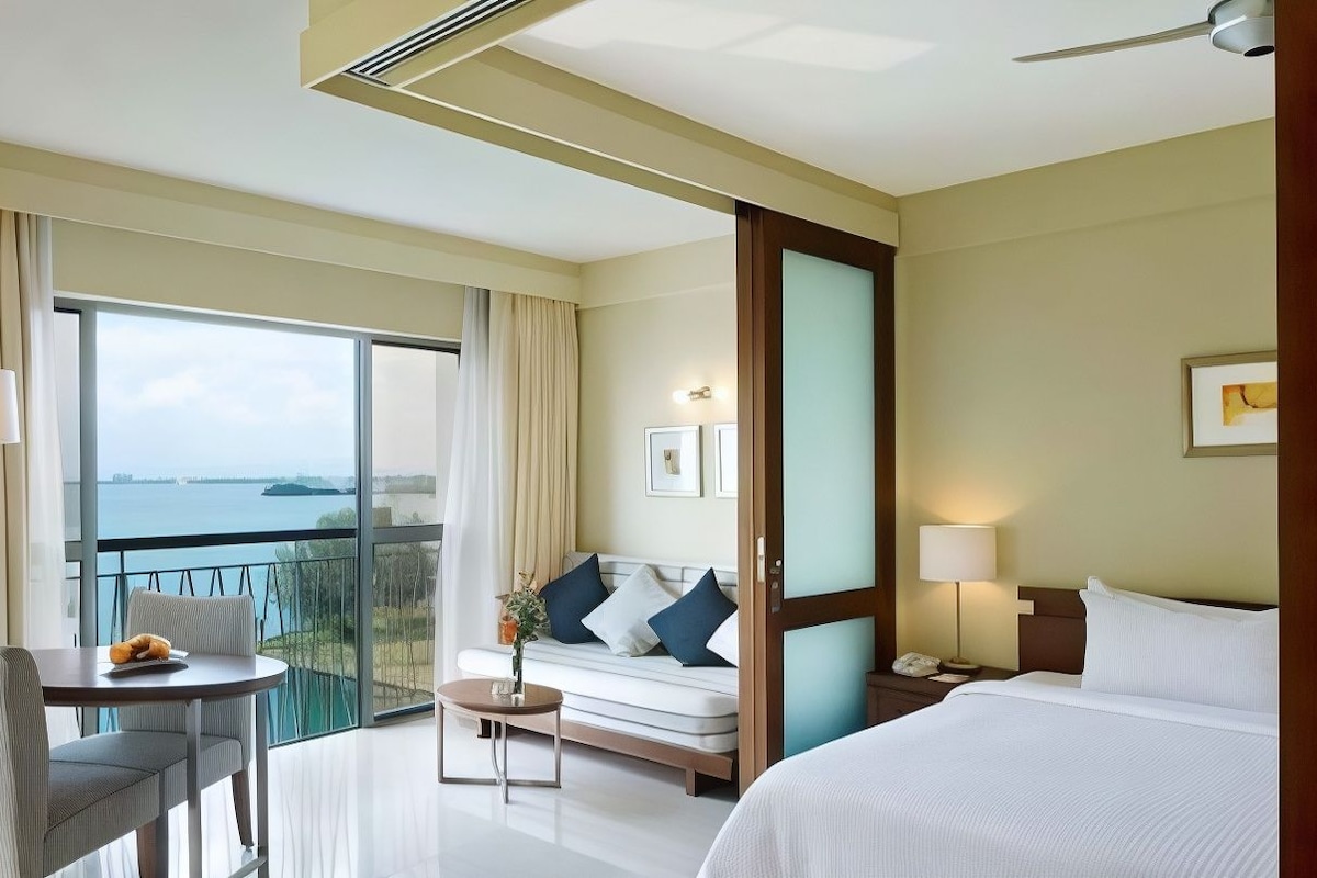 A hotel room with a bed, a sofa, a table, and a view of the water.